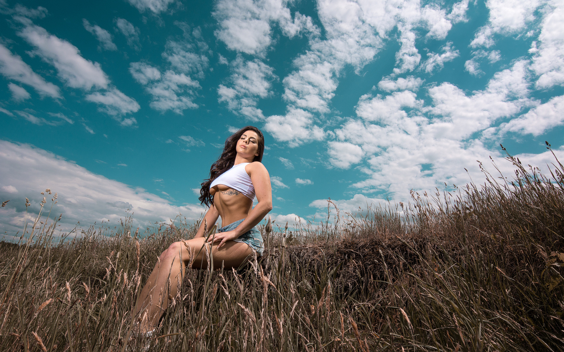 women, closed eyes, underboob, t-shirt, sitting, women outdoors, sky, clouds, tattoo, long hair, wavy hair, belly, brunette, boobs, jean shorts