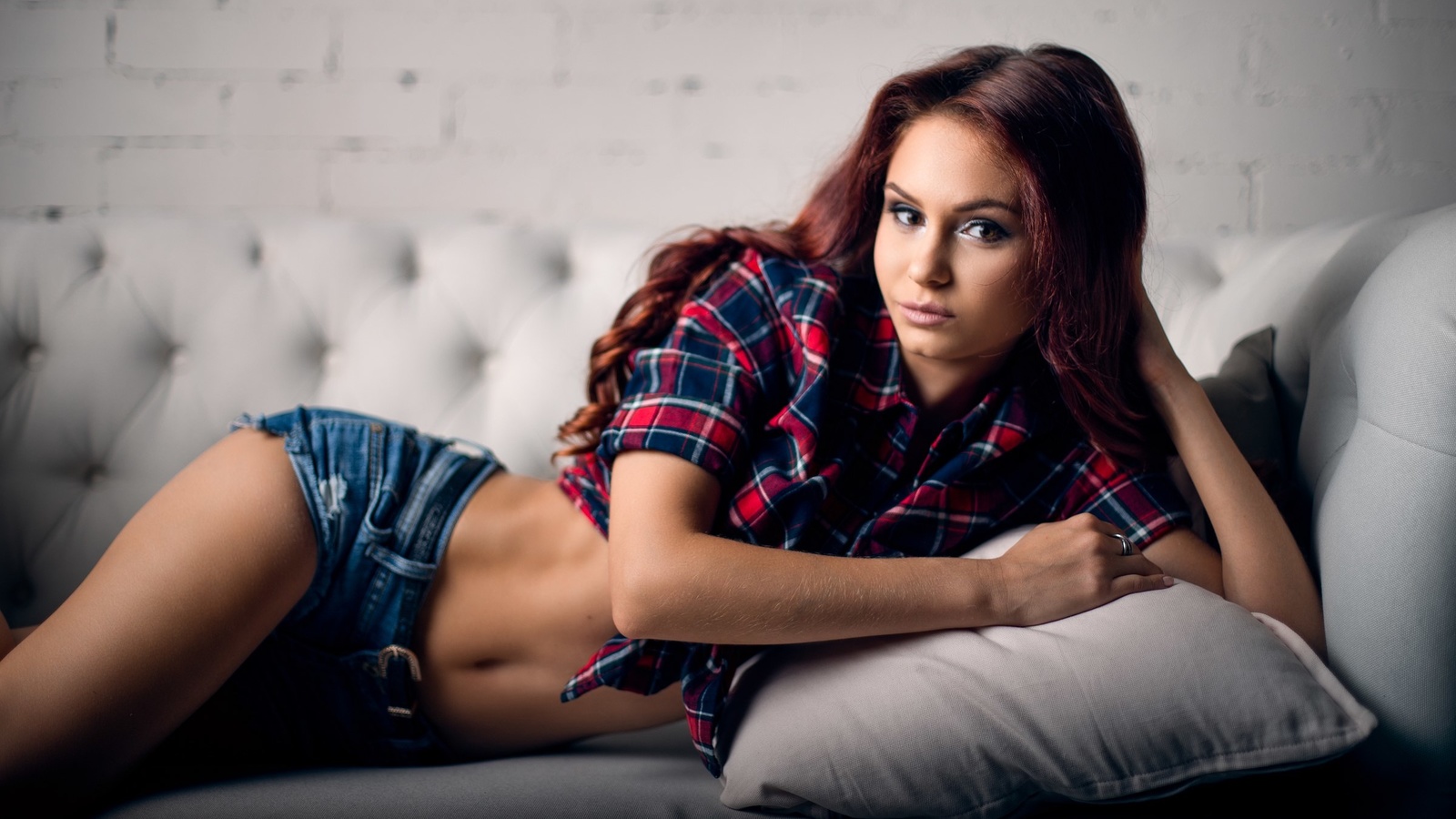 women, tanned, jean shorts, plaid shirt, belly, couch, pink lipstick, dyed hair, wall, bricks
