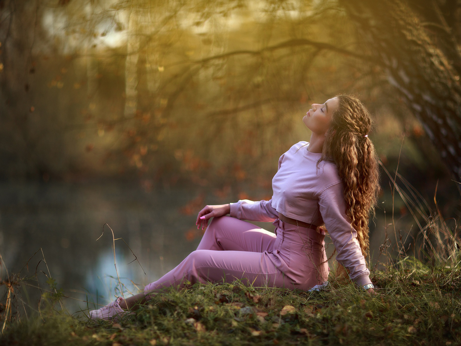 women, model, brunette, women outdoors, lake, nature, curly hair, wavy hair, sitting, sweater, pants, closed eyes, sneakers, trees, grass