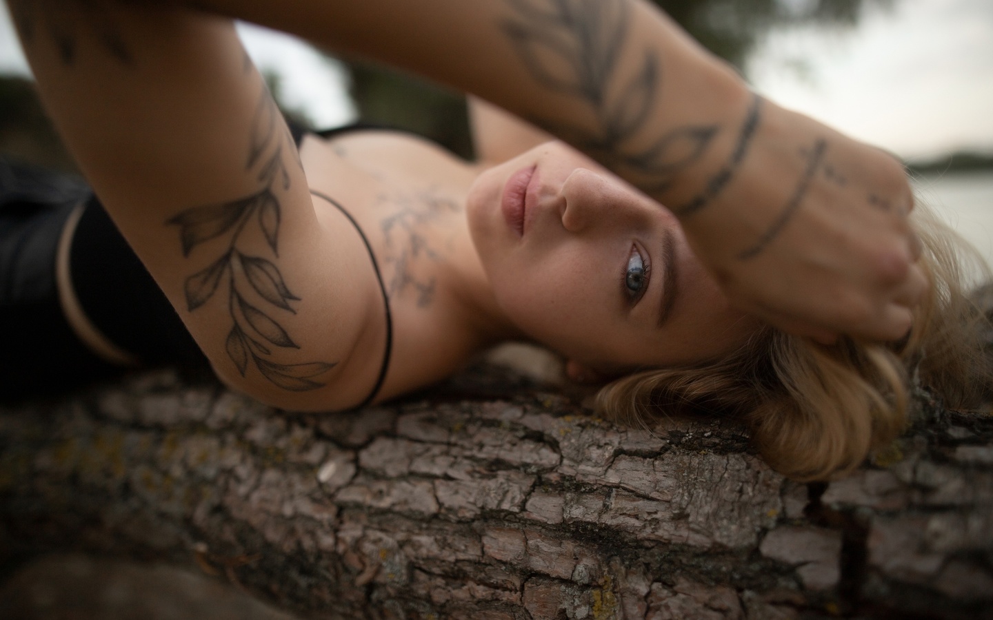 alexander nesterenko, tattoo, black top, blonde, nature, women outdoors, , trees, lying on back, model, tree trunk, sky, looking at viewer, clouds